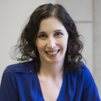 Alyssa Lederer smiles in a headshot. She is a fair skinned woman with dark brown hair and brown eyes. She wears a bright cobalt blue blouse.
