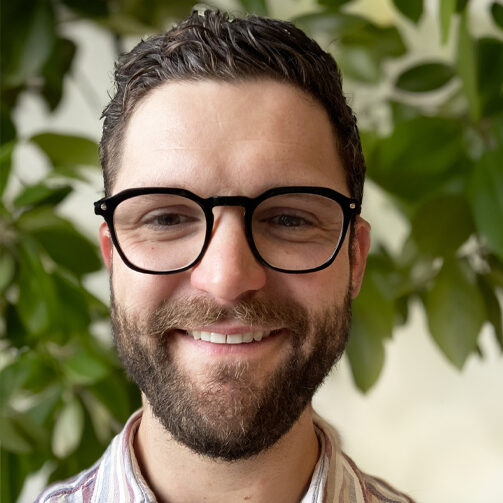 Davis Meadors smiles in a headshot. He is a younger white male, with brown hair in a close cut, a brown beard and mustache, and dark rimmed glasses.