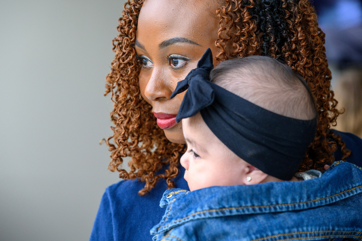 Joyce Adams holds an infant while looking at something off frame.