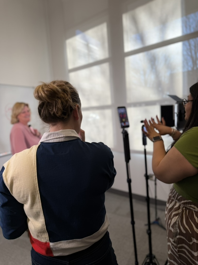 Sharon Moe is filmed while Bonnie gives direction behind a phone camera on a stand. Lynsey's back is in the foreground.