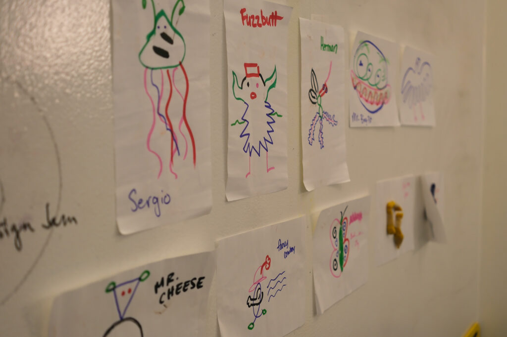 Colorful drawings in marker taped to a whiteboard.