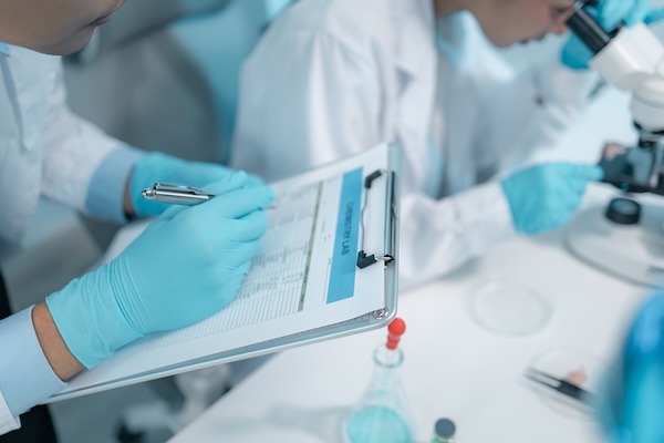 Clinical researchers review health record data and look at specimens under a microscope.