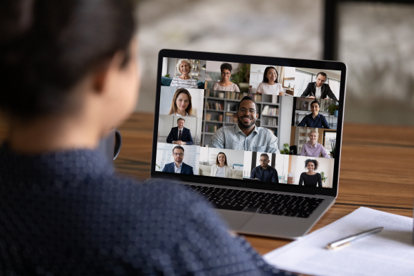 A person faces away from the camera, looking at a laptop screen of a virtual meeting space with many people on the screen.