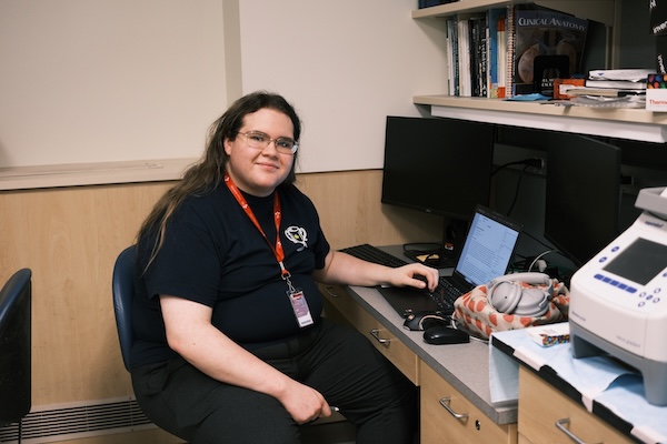 Solis Kent, seated, poses next to a computer and lab equipment. He is smiling at the camera.