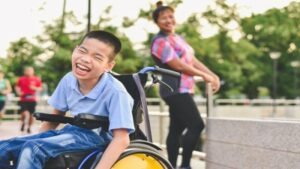 child in wheelchair with person standing behind