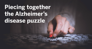 Picture of hand completing puzzle with the text "Piecing together the Alzheimer's disease puzzle"