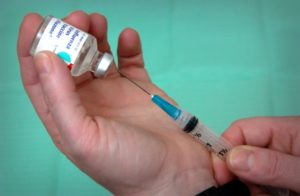 hands about to draw a vaccine into a syringe from a bottle of influenza vaccine