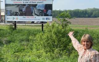 image of Debi Wallick gesturing excitedly towards new Hoosier Health and Wellness Alliance supported billboard