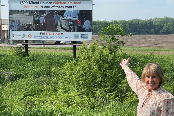 image of Debi Wallick gesturing excitedly towards new Hoosier Health and Wellness Alliance supported billboard