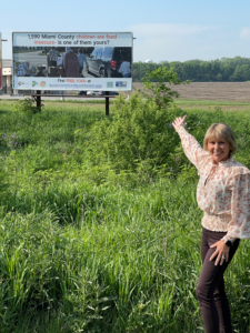 image of HHWA partner Debi Wallick standing and gesturing excitedly towards a billboard about food insecurity in Miami County, Indiana