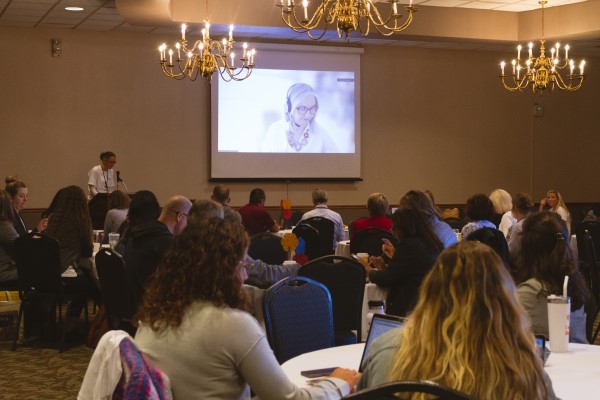 a crowd of attendees at the 2022 CHeP community engagement day views keynote speaker on the screen at the head of the room