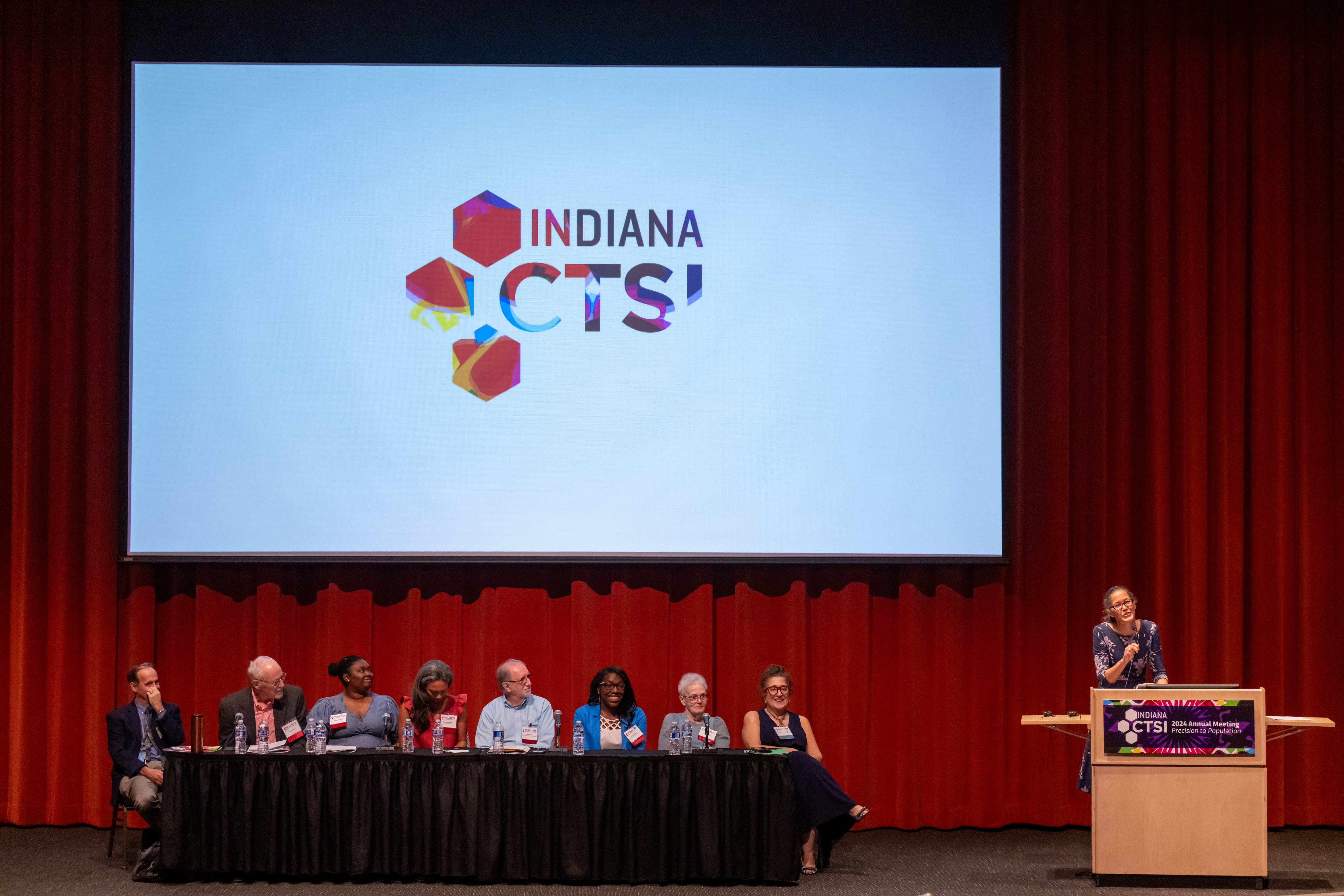 Dr. Sarah Wiehe stands in front of a panel that includes researchers and community members.