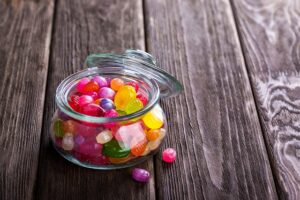 Image shows a glass candy jar with jelly beans against a wooden table