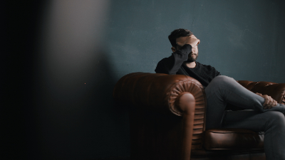 photo of a man sitting on a couch with his hand to his forehead