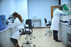 Image shows two black doctors working in a lab, leaning over white lab equipment.