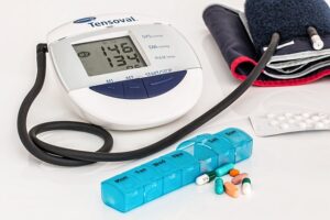 image shows a blood pressure monitor and a pill box in the foreground