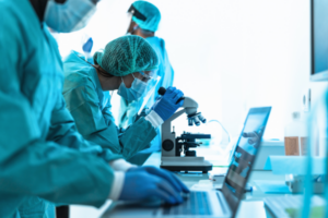 Image of researchers in ppe working in a laboratory, looking at a computer screen and a microscope.