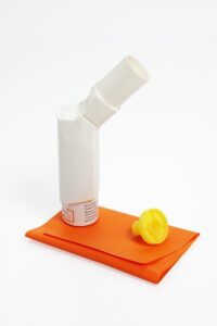 image shows an inhaler with spacer sitting over an orange cloth