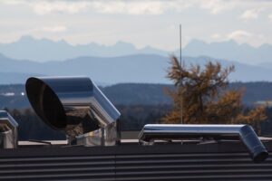 Image shows an air vent atop a building with mountains in the backdrop