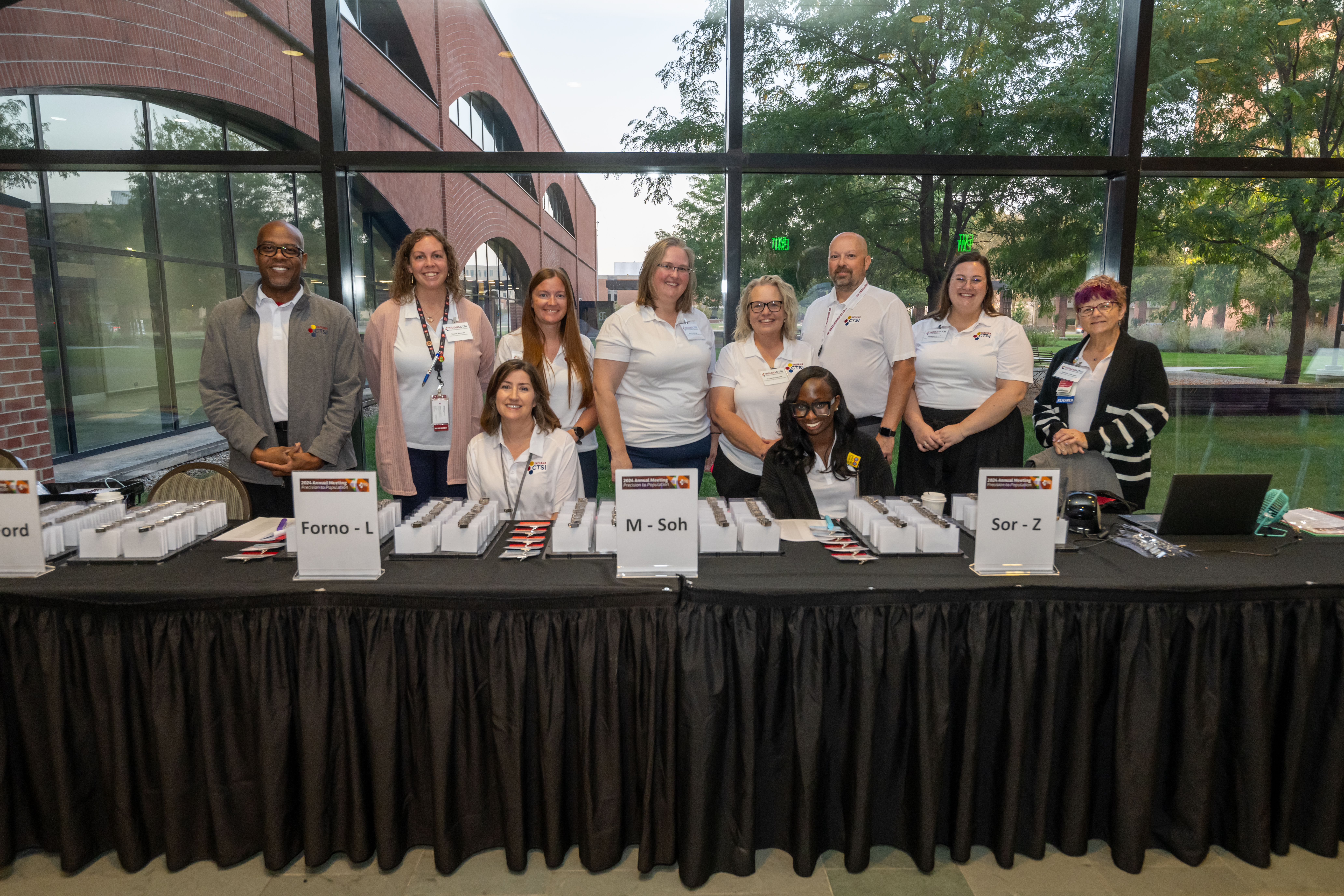 The 11 volunteers who helped to make the 2024 Annual Meeting possible all pose together as a group at the main check-in table. 